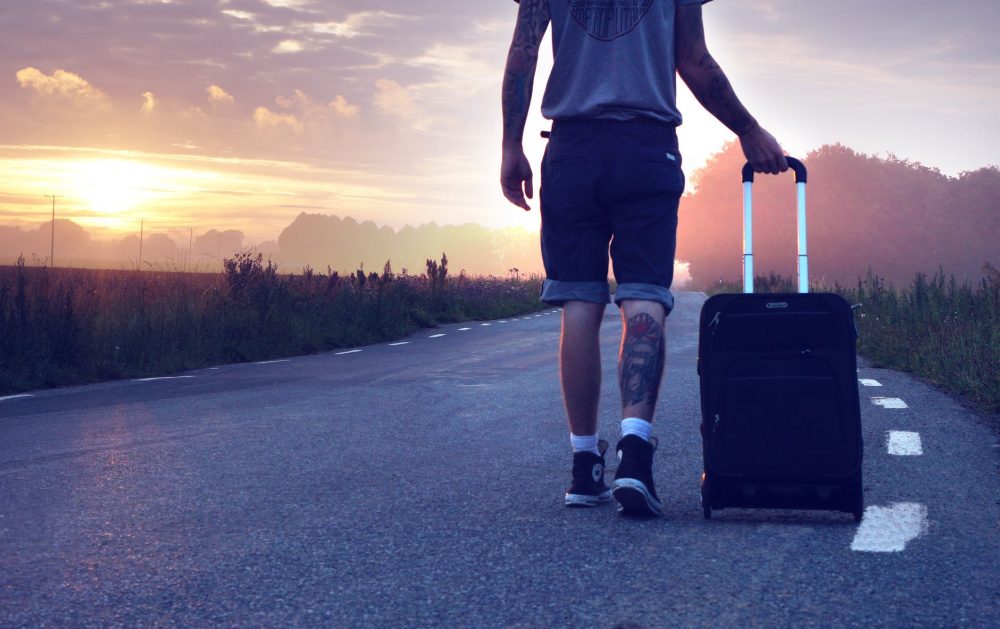 man with luggage on road during sunset