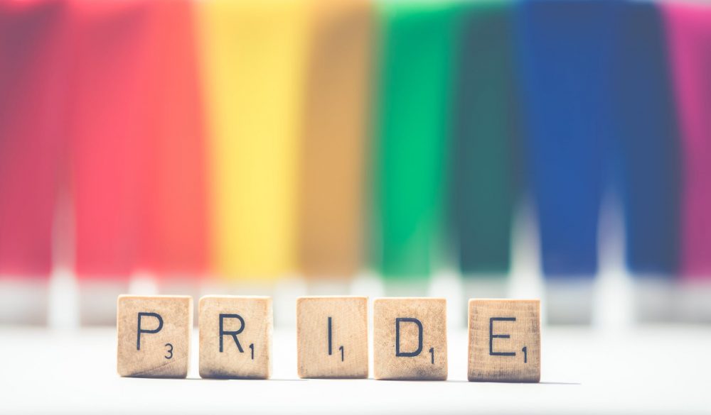 selective focus photography of scrabble pride on white and multicolored background